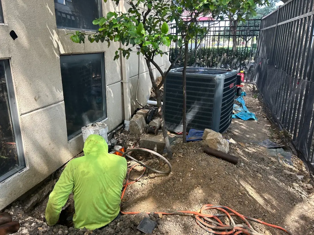 Crew member working in a hand-dug pier excavation along a building exterior