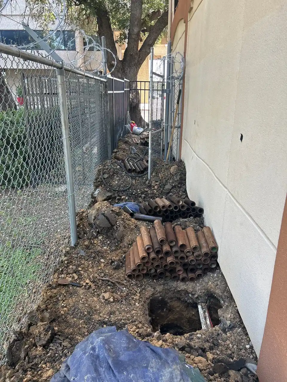 Steel pier pipe sections staged along a perimeter excavation at a building wall